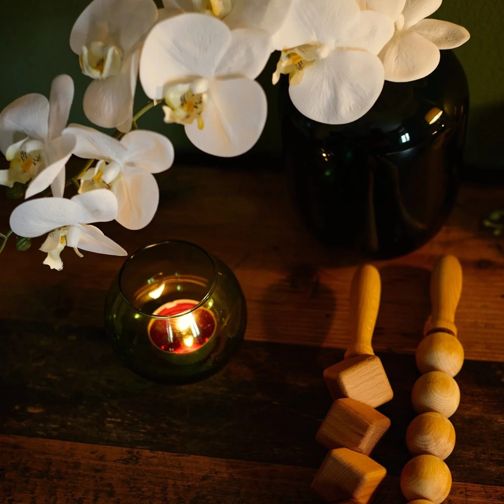 Foto di un tavolo con sopra dei fiori, una candela e dei bastoni per dei massaggi. La foto è stata realizzata presso Benessere Musaj